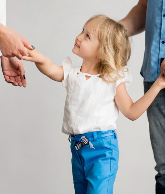 Małżonkowie po rozwodzie stoją oddaleni od siebie, a pomiędzy nimi jest dziecko, które trzymają za ręce. Matka utrudniająca ojcu kontakty z dzieckiem